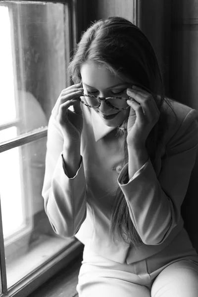 Ritratto di giovane bella ragazza in occhiali sul davanzale della finestra. Foto in bianco e nero — Foto Stock