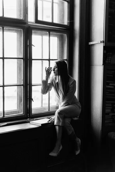 Bela senhora de negócios elegante em óculos lê um livro no peitoril da janela. Foto em preto e branco — Fotografia de Stock