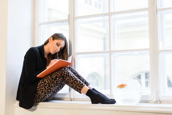 Menina bonita e elegante lendo um livro no peitoril da janela — Fotografia de Stock