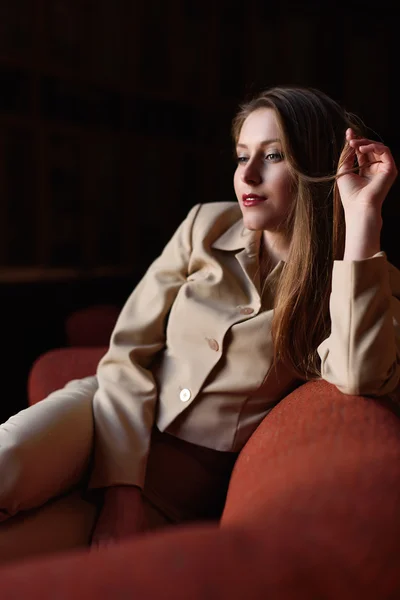 Portret van mooie stijlvolle jongedame in pak zittend op de rode sofa — Stockfoto