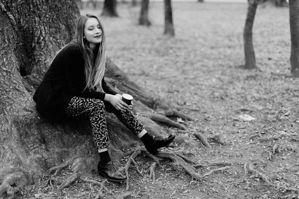 Elegáns fiatal lány ül a fa tavaszi park közelében. Fekete-fehér — Stock Fotó