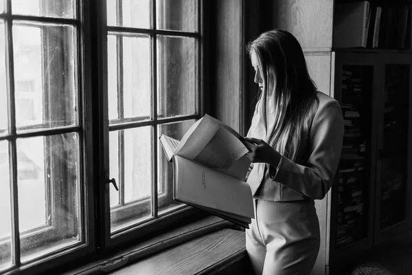美丽的时尚年轻女孩读一本书复古窗口在图书馆附近。黑白照片 — 图库照片