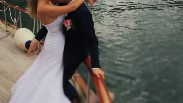 Charmante mariée blonde et beau marié s'embrassant passionnément sur le yacht avec les montagnes et la mer en arrière-plan — Video