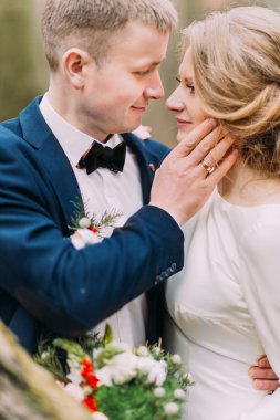 Yakışıklı damat yavaşça gelini doğa arka plan üzerinde yüz dokunur