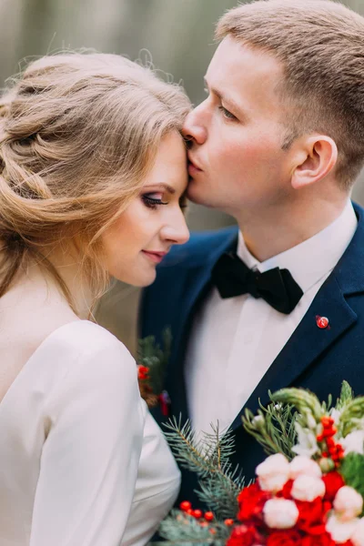 Close up retrato de noivo elegante beijando sua bela noiva na testa. Dia ensolarado na floresta — Fotografia de Stock