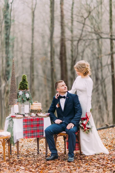 Beau couple de mariage posant près de la table décorée pour les vacances de Noël dans la forêt d'automne . — Photo