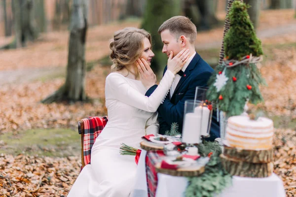 秋の森の休日テーブルでお互いの顔をそっとなでる魅力的な結婚式のカップル — ストック写真