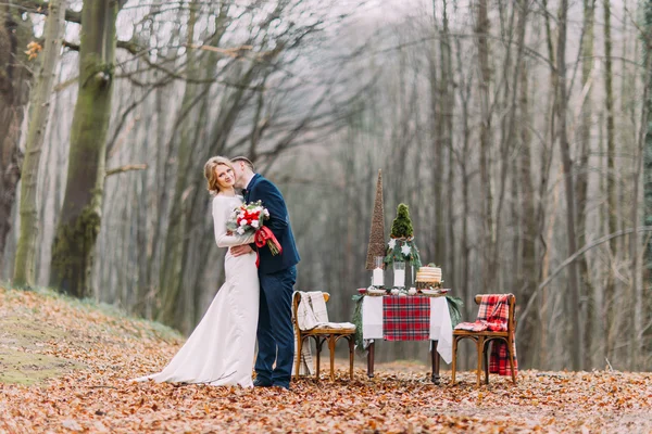 Pareja de bodas cerca de la mesa decorada para las vacaciones de Navidad en el bosque de otoño . — Foto de Stock