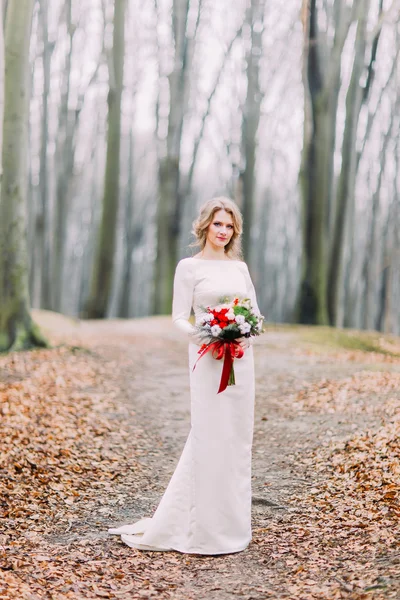 Glücklich schöne blonde Braut auf dem herbstlichen Wald mit Strauß roter Blumen — Stockfoto