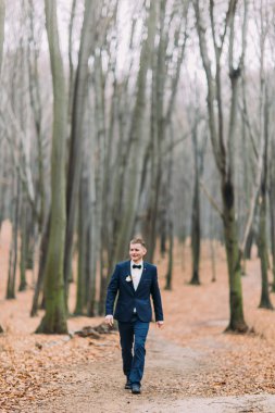 Kendine güvenen genç damat şık elbiseli sonbahar orman yürür