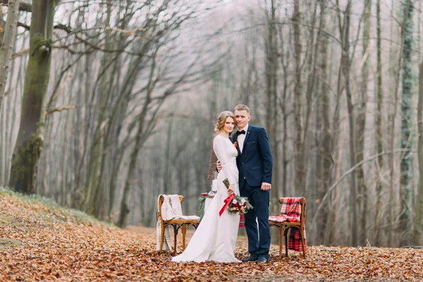 Schönes Hochzeitspaar posiert neben dem geschmückten Weihnachtstisch im herbstlichen Wald. — Stockfoto