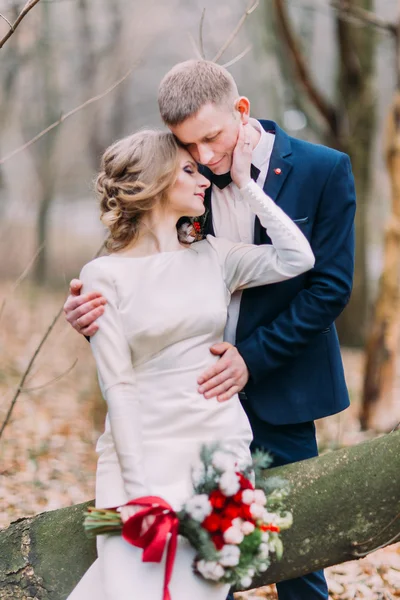 Beautiful young wedding couple sitting on the stump and hugging in autumn forest — Stock Photo, Image