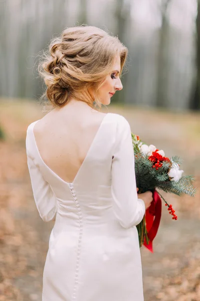 Bela noiva loira no vestido de noiva de renda longa segurando buquê na floresta de outono visão traseira — Fotografia de Stock