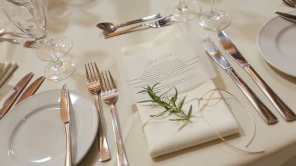 Свадебный стол накрыт для празднования: тарелки, вилки, белая скатерть с цветочными украшениями — стоковое видео