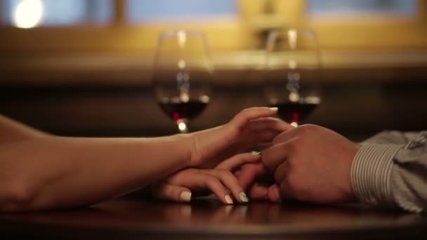 Close up of loving couple holding hands during romantic dinner. Glasses of red wine on background — Stock Video