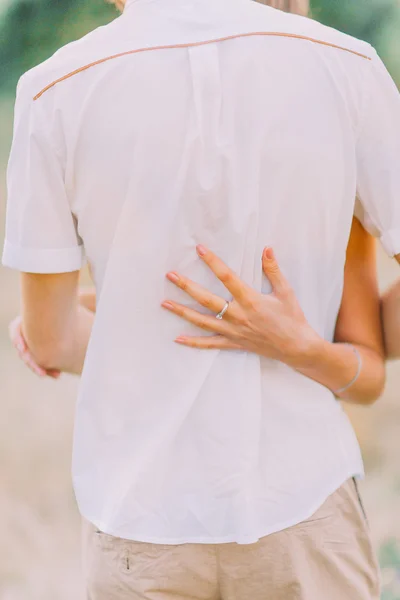 Close up hands of attractive young couple on a date walking together in park, hugging each other around the waist, back view