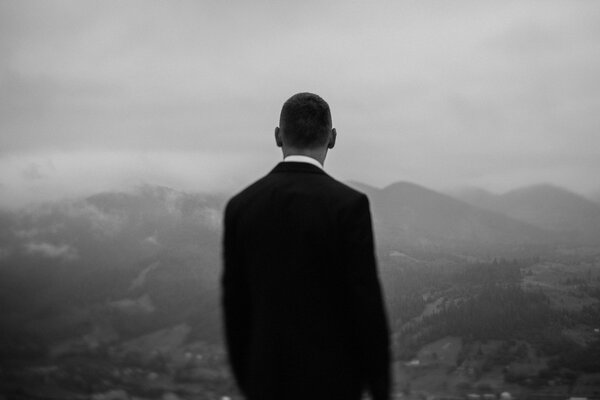 Handsome young groom standing in front of mountains and looking at nature