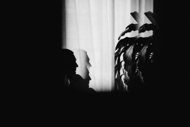 Mysterious man sitting with shadows by the window. Dark background