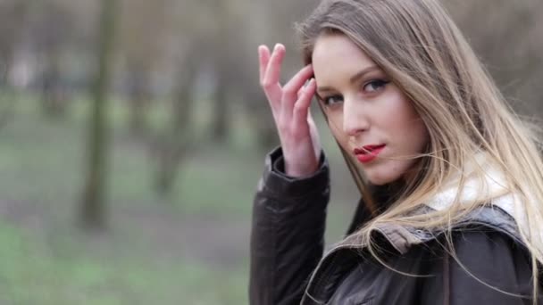 Jonge stijlvolle hipster meisje met rode lippen zacht aanraken mooi gezicht en corrigeert kapsel. Herfst park achtergrond. Video in slow motion — Stockvideo