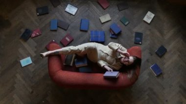 Birçok kitap ve eğlenceli gülümseyerek çevrili kırmızı kanepeüzerinde gözlük çekici rüya gibi kız