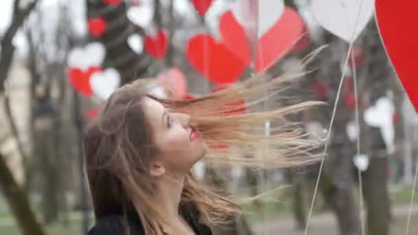 Stílusos szőke lány játszik vörös papír szív dekoráció az őszi parkban. Valentin-nap ünnepe