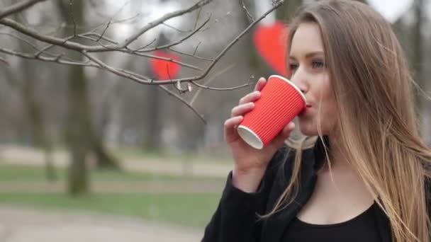 Retrato de una hermosa joven de moda urbana en el parque de otoño bebiendo una taza de café para llevar — Vídeo de stock