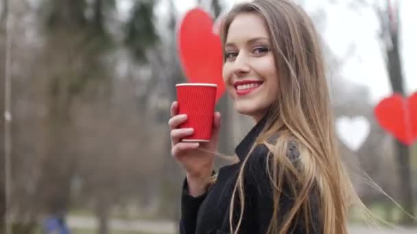 Junge schöne blonde Hipster-Frau posiert auf dem Herbst Park Hintergrund mit einer Tasse Kaffee zum Mitnehmen — Stockvideo