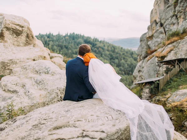 Casamento casal suavemente abraçando em montanhas rochosas contra o céu. Momento romântico bonito. Visão traseira — Fotografia de Stock