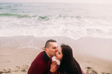 Yakın yüz portre aşık güzel genç çift plajda oturan ve öpüşme. Kış denizi arka plan