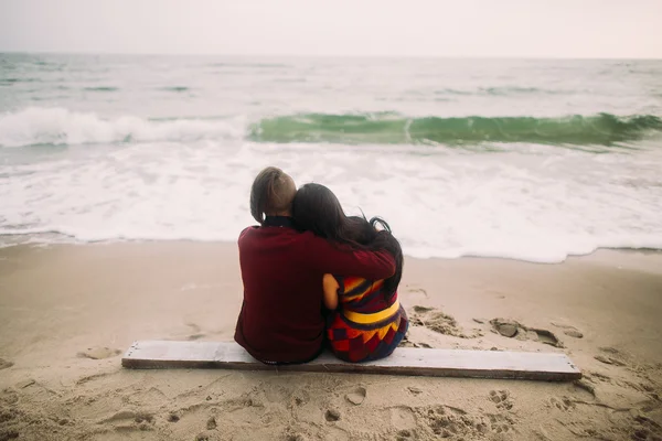 Досить молода пара сидить на пляжі і приймає. Зимовий морський фон. Ніжний момент. Вид ззаду — стокове фото