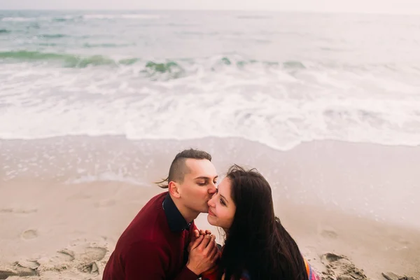 Close up face portrait of beautiful young couple in love sitting on the beach and kissing. Winter sea background — Stock Photo, Image