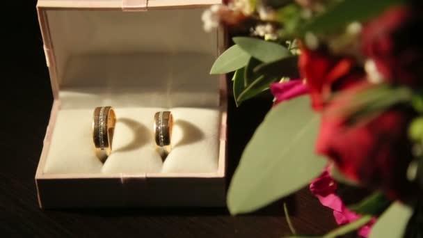 Samenstelling van rode doos met gouden glanzend trouwringen en rode rozen op voorgrond — Stockvideo