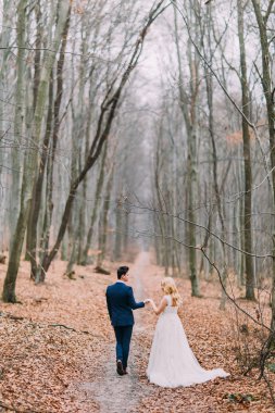 Happy wedding couple walks on the path in autumn forest