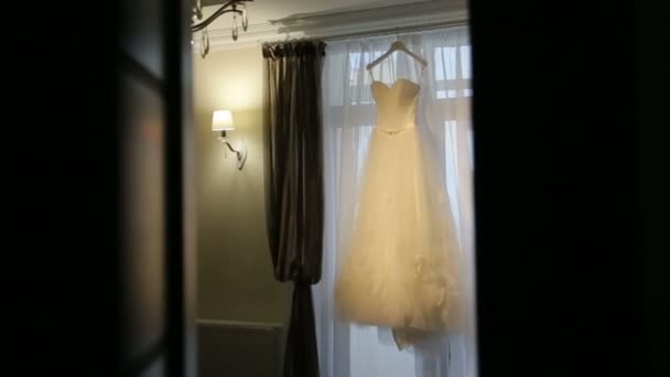 Beautiful white luxury wedding dress on hanger on the background of a window — Stock Video
