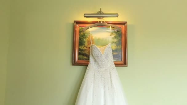 Белое кружевное свадебное платье висит на зеленом фоне стены. Свадебная подготовка — стоковое видео