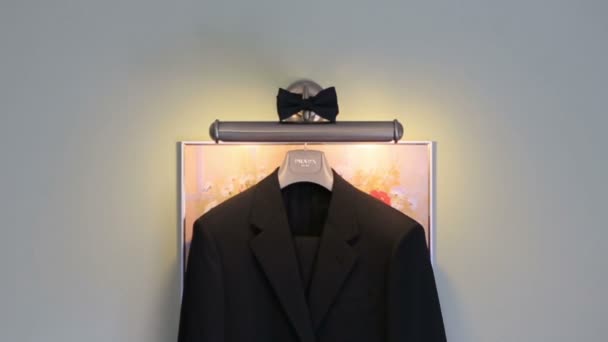 白い壁に蝶ネクタイの黒いウェディングスーツが掛かっています。結婚式のコンセプト — ストック動画