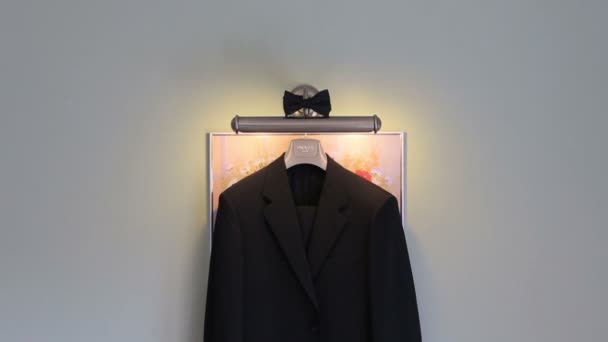 Stylish black wedding suit with bow-tie hangs on the  hanger. White wall background. Wedding concept — Stock Video