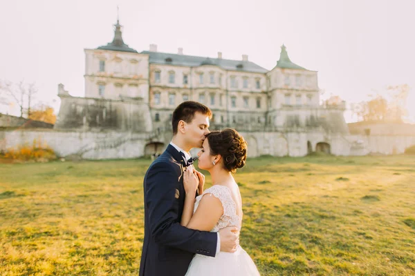 Glücklicher Bräutigam küsst Bräute auf die Stirn im Hintergrund alte Burg — Stockfoto