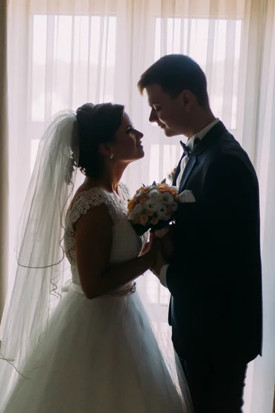 Piękne młode małżeństwo stoi przez okno obejmując twarzą w twarz — Zdjęcie stockowe