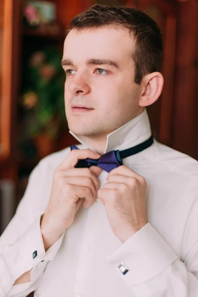 Close-up retrato de empresário bonito em terno azul colocando em arco-gravata dentro de casa — Fotografia de Stock