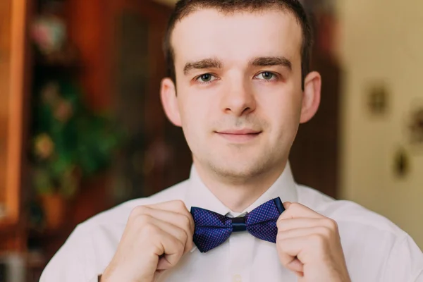 Joyeux jeune homme bien habillé fixant son noeud papillon souriant joyeusement à la caméra — Photo