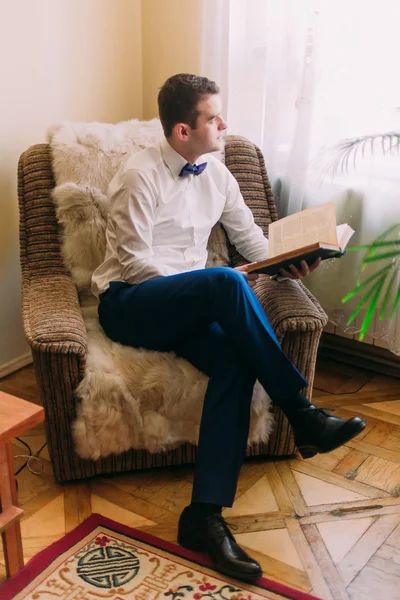 Jovem homem adulto de terno azul e camisa branca olhando para a distância com um livro em sua mão — Fotografia de Stock