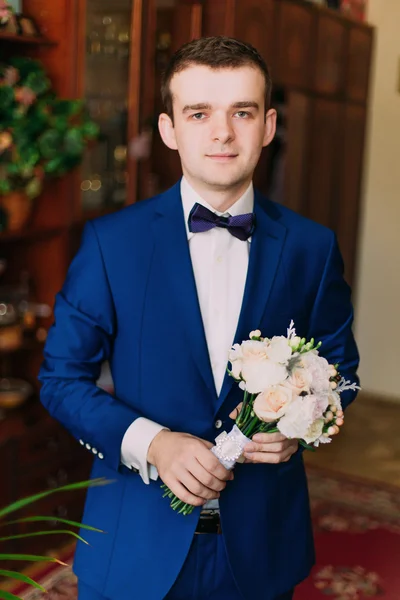Imut gaya pengantin pria dalam setelan biru dan dasi kupu-kupu dengan karangan bunga mawar — Stok Foto