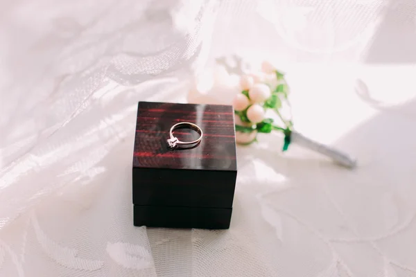 Golden wedding ring in box and rose flowers on the side. — Stock Photo, Image