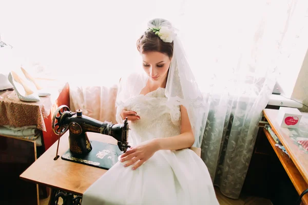 Hermosa novia joven hace ajustes de última hora a su vestido de novia en una antigua máquina de coser de banda de rodadura —  Fotos de Stock
