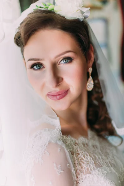 Primer plano retrato de la feliz novia sonriente en vestido blanco de lujo y velo posando con rosa cerca de la ventana —  Fotos de Stock