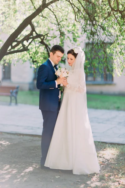 Couple amoureux mariée et marié regarder bouquet nuptiale de roses blanches à l'extérieur — Photo