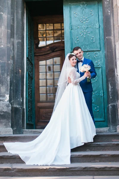 Belle jeune mariée élégante et beau marié tenant bouquet de roses en plein air château porte arrière-plan — Photo