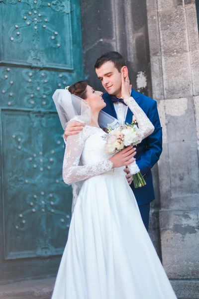 Belle jeune mariée élégante et beau marié tenant bouquet de roses étreignant face à face à l'extérieur château porte arrière-plan — Photo