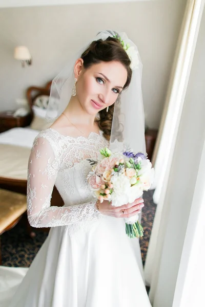 Close up retrato de noiva elegante feliz em vestido branco de luxo e véu posando com rosas cor de rosa perto da janela — Fotografia de Stock